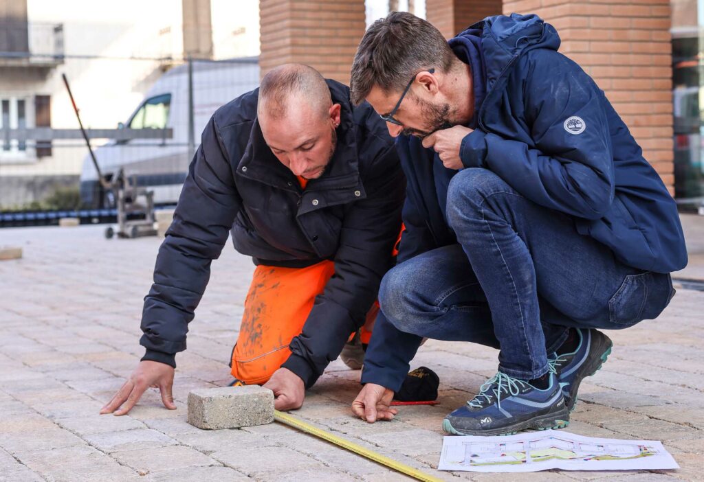 Due lavoratori di Acerbis Paesagistica mentre effettuano misurazioni sul terreno, illustrando l'attenzione al dettaglio nella fase di progettazione.